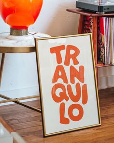 an orange and white sign sitting on top of a wooden floor next to a table