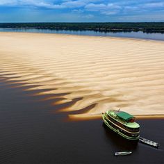 a green boat floating on top of a river next to a sandy shore covered in sand