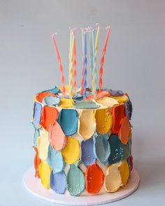 a multicolored birthday cake with candles on it's top and frosting