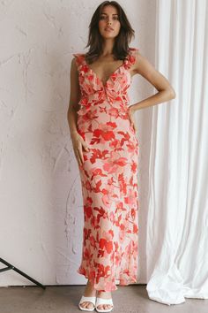 a woman standing in front of a white wall wearing an orange and pink floral dress