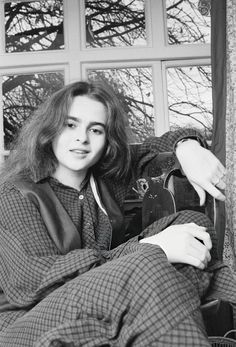 a black and white photo of a woman sitting in front of a window