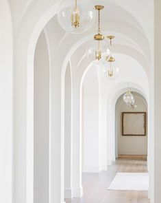 an empty hallway with arches and chandeliers on either side of the corridor is shown