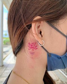 a woman with a pink flower tattoo on her left side behind her ear is looking away from the camera