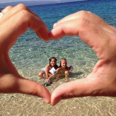 two people making a heart shape with their hands on the beach in front of them