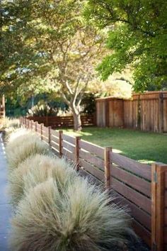 the grass is growing on the side of the road next to the fence and trees