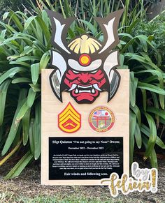 a sign with an image of a demon on it in front of some plants and bushes