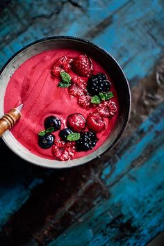 a bowl filled with berries and blueberries on top of a wooden table next to a knife