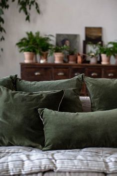 two green pillows sitting on top of a bed next to a wooden dresser with potted plants