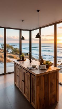 a kitchen with an island in front of large windows overlooking the ocean and beach at sunset