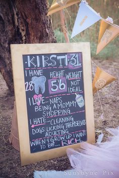 a chalkboard sign that has been decorated with balloons and streamers in front of a tree