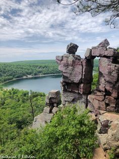 some rocks and trees on a hill overlooking a body of water with clouds in the sky