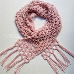 a pink crocheted scarf with tassels on the ends is laying on a white surface