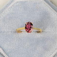 an oval shaped pink tourmaline stone sits on top of a gold band ring