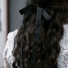 the back of a woman's head with long curly hair wearing a black ribbon