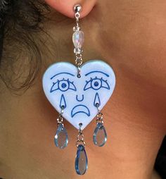 a close up of a person wearing earrings with faces drawn on them and tear drops dangling from the ear