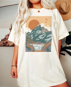 a woman standing in front of a wall wearing a t - shirt with mountains on it