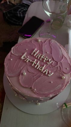 a pink birthday cake sitting on top of a table next to a glass of wine