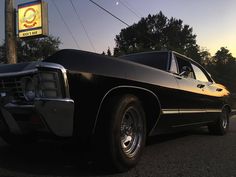 an old black car is parked in front of a gas station sign and some trees