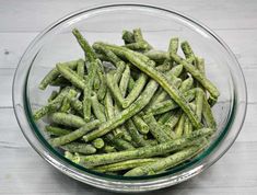 a glass bowl filled with green beans on top of a wooden table