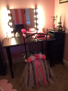 a desk with a mirror, chair and lights in the corner on top of it