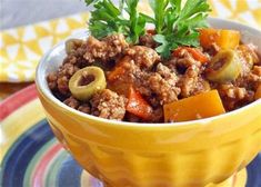 a yellow bowl filled with meat and vegetables on top of a colorful place mat next to a fork