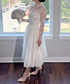 a woman standing in front of a window holding a bouquet of flowers and looking out the window