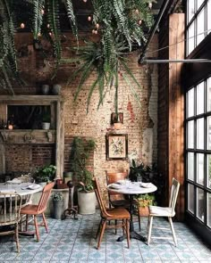 an indoor dining area with brick walls and potted plants hanging from the ceiling, surrounded by large windows