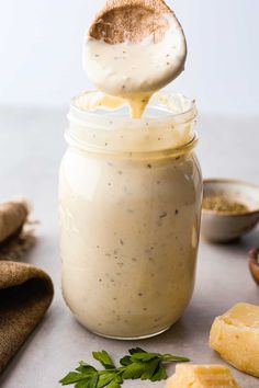 a spoon full of dressing being drizzled over the top of a jar