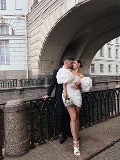 a man and woman standing next to each other in front of a building on a bridge