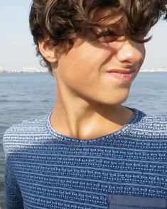 a young man standing in front of the ocean with his hair blowing back and eyes closed