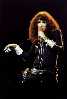 a woman with red hair and makeup holding a microphone in her right hand while standing on stage