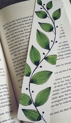 two bookmarks with green leaves on them are laying next to an open book,