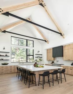 a large kitchen with an island and wooden cabinets in the center is surrounded by black chairs