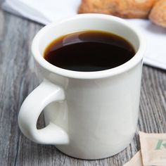 a cup of coffee sitting on top of a wooden table next to some croissants