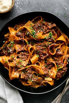 a black bowl filled with pasta and meat on top of a table next to a glass of wine