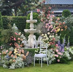 a garden filled with lots of flowers next to a white chair and water fountain on top of a lush green field