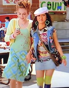 two women walking down the street with cell phones in their hands and one is wearing a sailor's hat