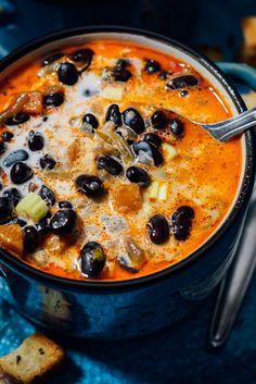 a close up of a bowl of soup with olives and bread on the side