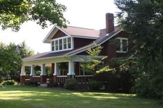 a large brown and white house sitting in the middle of a lush green field next to trees