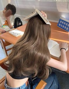 a woman sitting at a desk with an open book on top of her head