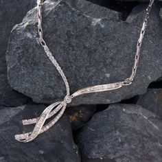 This bejeweld 14k white gold necklace features a ribbon motif accented with one (1) bezel set round brilliant cut diamond, thirty-nine (39) prong set round brilliant cut diamonds, and thirty-five (35) channel set baguette cut diamonds. The pendant measures 57mm by 52mm and is attached to a fancy link chain.  The overall length of the necklace is 17.5 inches. Channel Set Cubic Zirconia Anniversary Necklaces, Anniversary Cubic Zirconia Channel Set Necklace, Gift Channel Set Diamond Necklace In White Gold, Elegant Pave Setting Diamond Necklace For Anniversary, Diamond White Necklaces With Channel Set For Anniversary, Silver Channel Set Diamond Necklace For Anniversary, Diamond White Channel Set Necklaces For Anniversary, Diamond White Channel Set Necklace For Anniversary, Anniversary Channel Set Cubic Zirconia Necklace