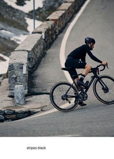 a man riding a bike down the side of a road next to a stone wall