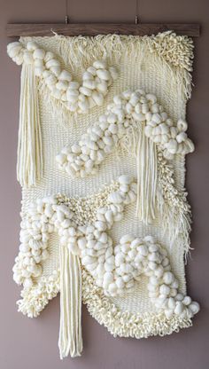 a wall hanging with white yarn and tassels