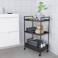 three tiered shelving unit in a bathroom with white tile walls and flooring