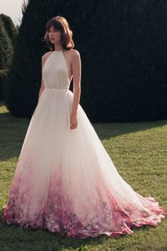 a woman in a white and pink dress standing on the grass with her hands behind her back