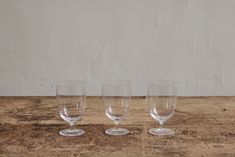 three empty wine glasses sitting on top of a wooden table next to a white wall