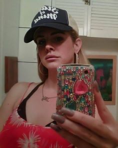 a woman holding a cell phone and wearing a baseball cap while standing in front of a mirror