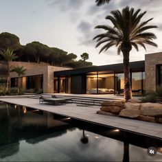 a large pool surrounded by palm trees next to a house with glass doors and windows