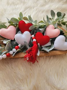 some red and white hearts are on a wooden board with greenery, berries and leaves