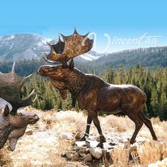 two moose statues in the middle of a field with pine trees and mountains in the background